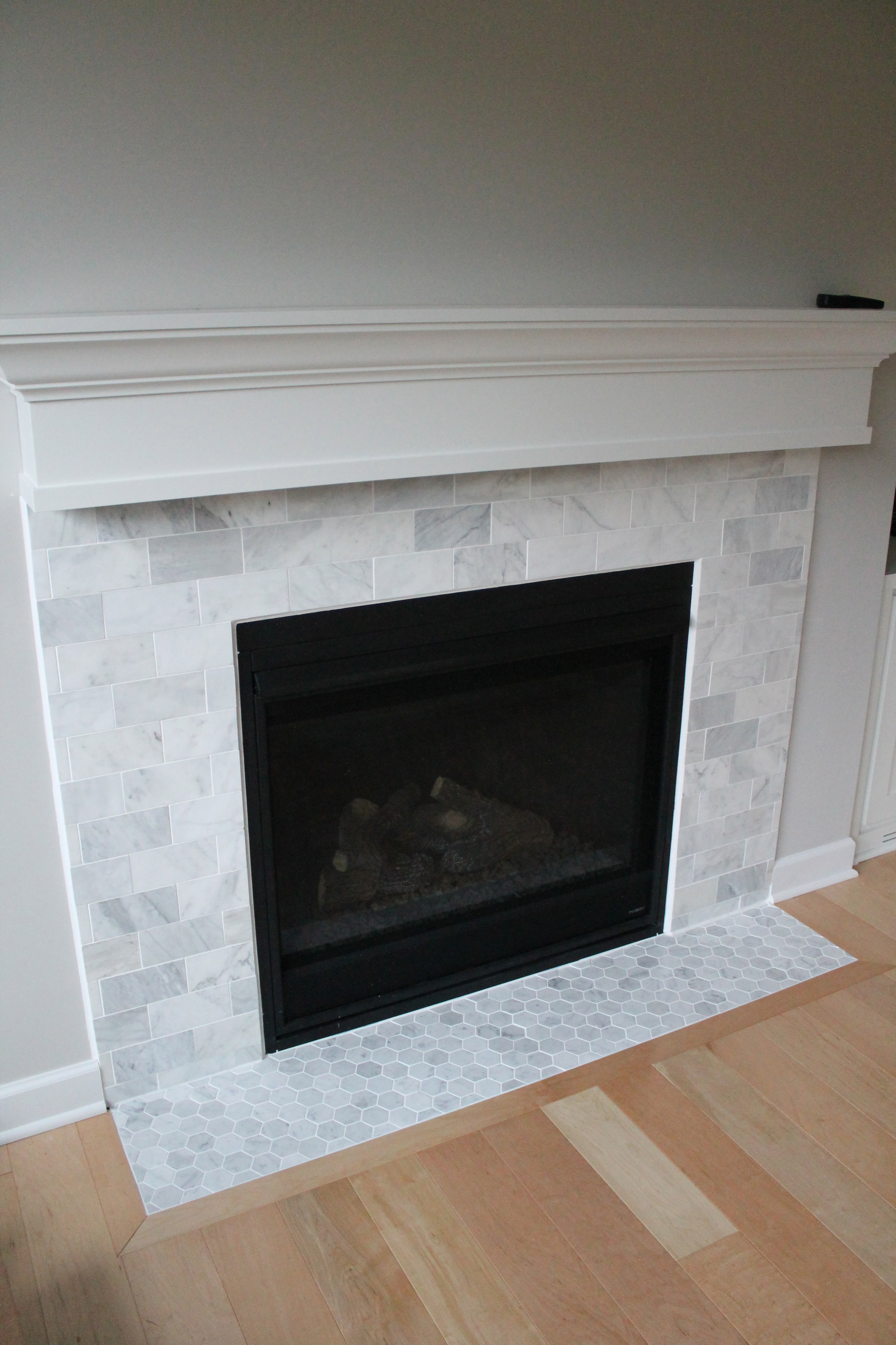 Marble tiles are a common way to add beauty to fireplaces. White is always a marketable and classic color. It is a bright color that reflects light and cleanliness. And marble is an ideal material for low traffic areas like fireplace surrounds. So this tile was a perfect choice!