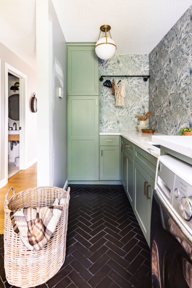 a photo of a bold laundry/mudroom with black herringbone tile and signature wallpaper, the cabinetry is painted in dried thyme | 2025 interior design trends 