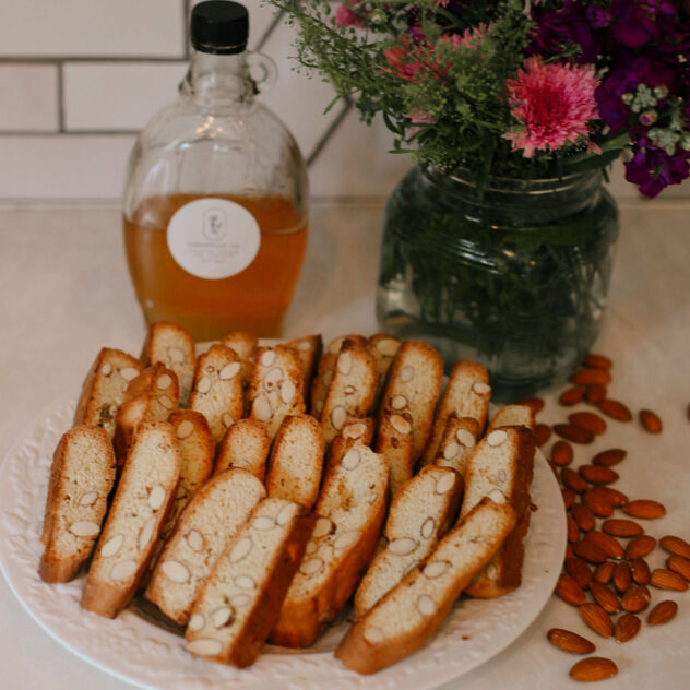 a plate full of freshly baked almond biscotti with a jar of honey and a bouquet of flowers in the background