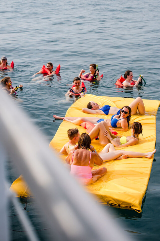 some female contractors are in their lifejackets swimming and others are floating on the aqua lily pad in the ocean during buildher retreat 