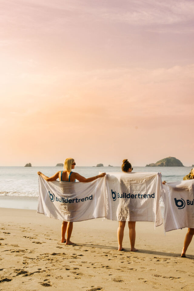 a photo of three female contractors holding buildertrend towels, facing the ocean in Costa Rica while attending buildher retreat 2025, organized by Morgan Molitor of construction2style