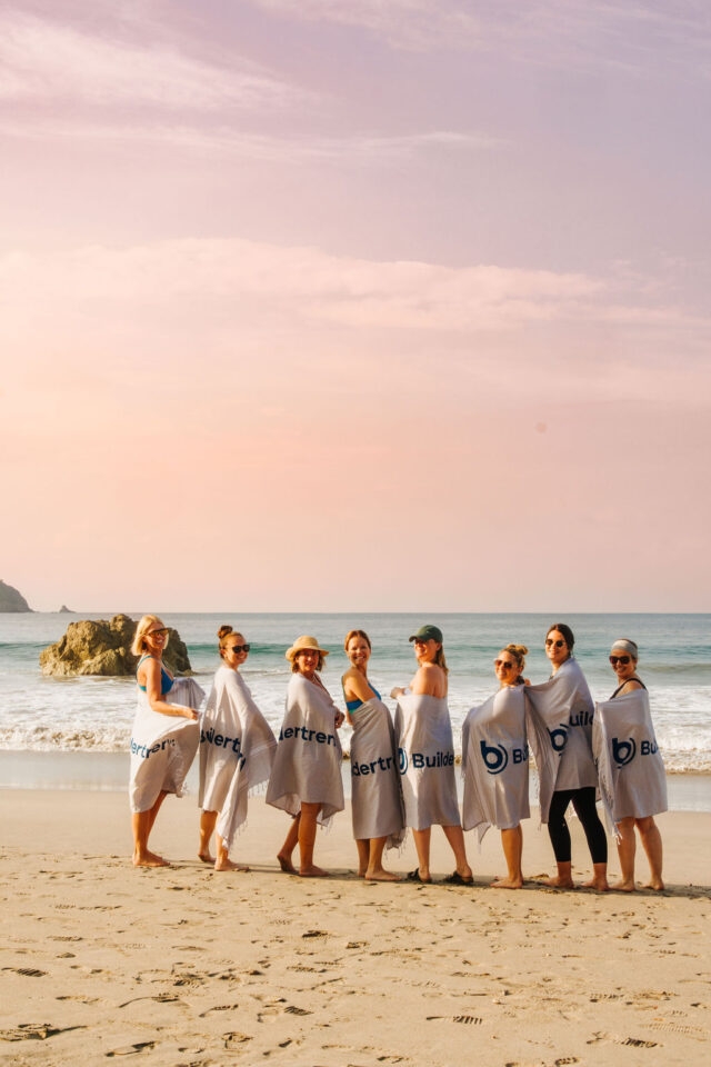 Morgan Molitor of construction2style and seven other female contractors on the beach in costa rica wrapped in buildertrend towels as buildertrend sponsored this contractor conference for women in 2025 