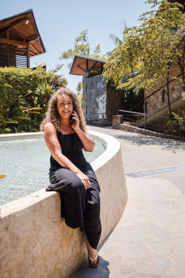 a photo of a female contractor speaking on the phone in front of the villa in costa rica while attending a contractor conference. for women 
