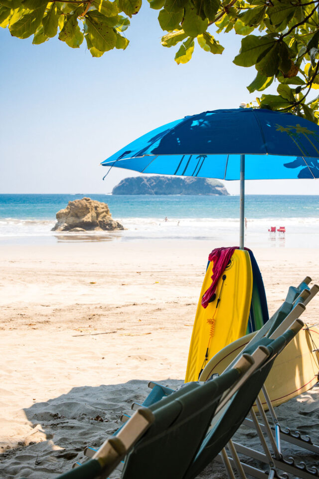 a photo of a yellow surf board under a blue umbrella at the beach in costa rica 