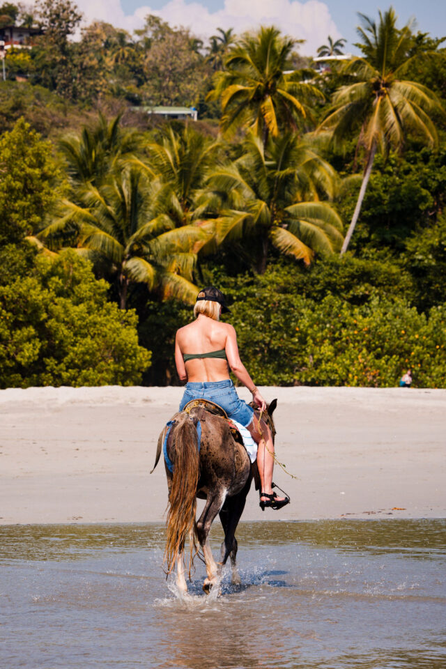 a photo of a female builder riding a horse on the beach in Costa Rica, heading towards the shore 