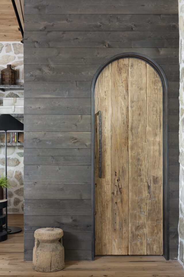 a look outside a half bathroom, showing shou sugi ban reclaimed wood paneling and a reclaimed wood door with natural stones accents off to the left