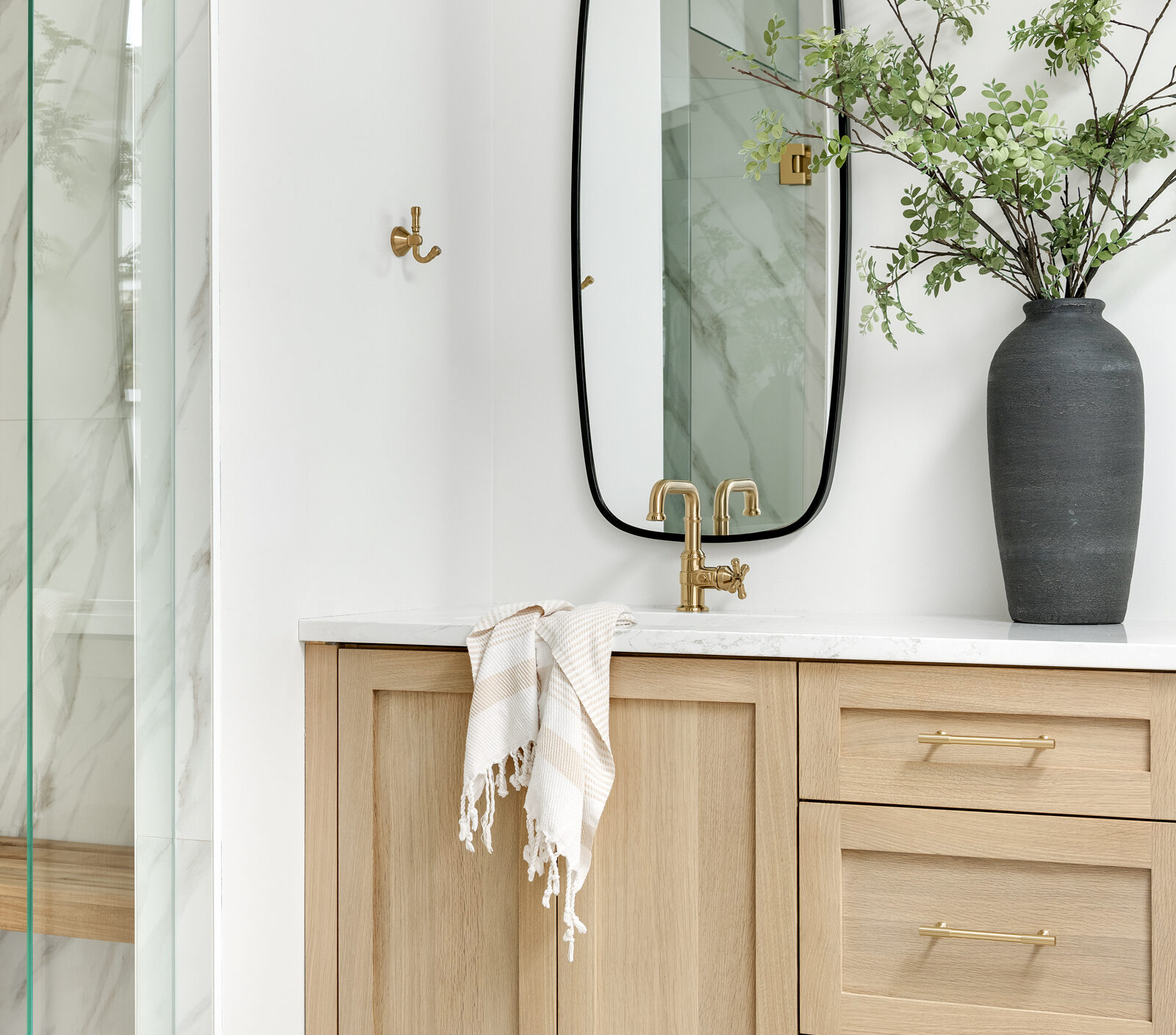 a photo of a primary bathroom designed and built by construction2style, it features a double vanity in rift sawn white oak finish, gold hardware, Rochester Accent Mirror placed vertically under an LED Bathroom vanity light