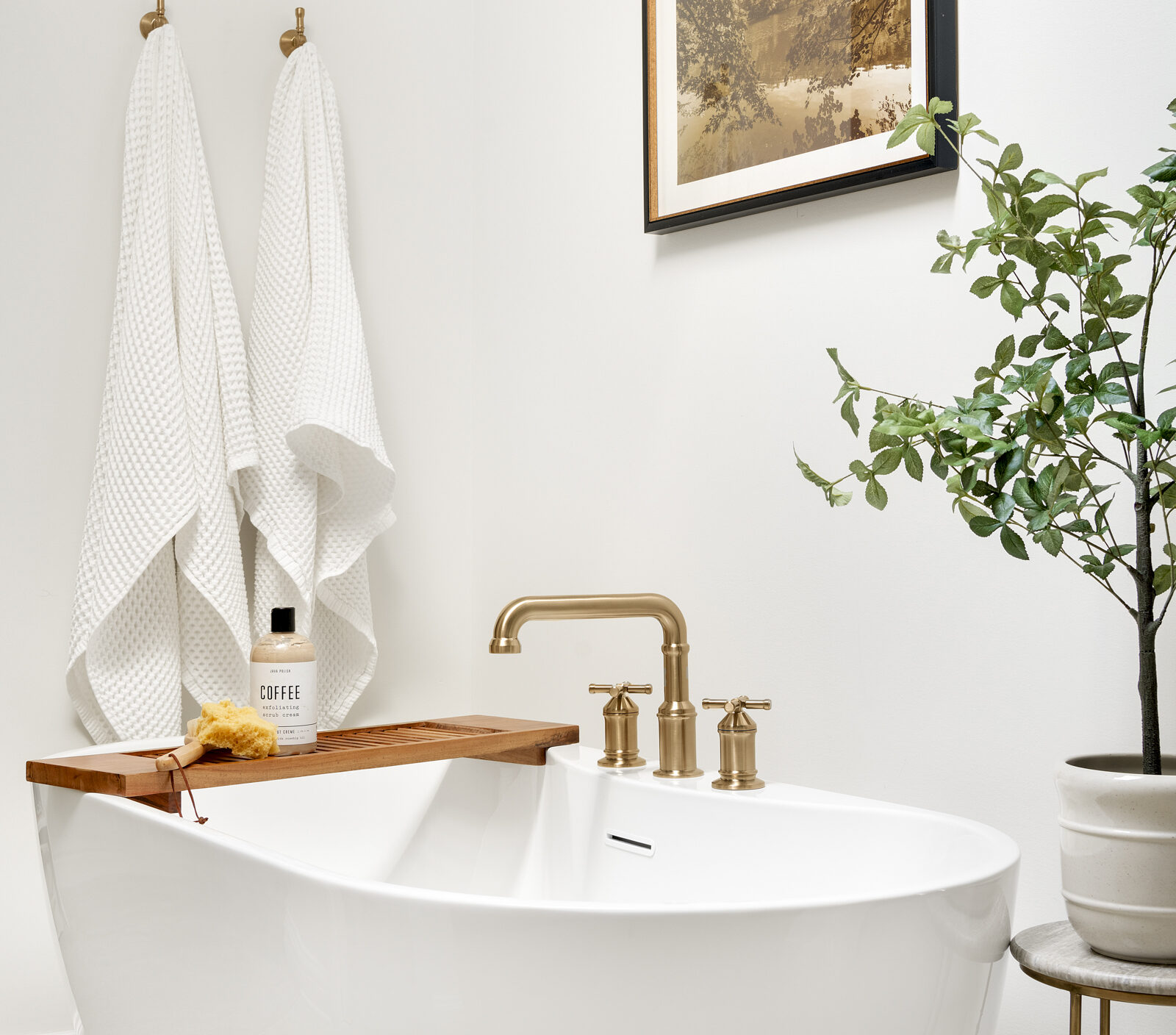 a photo of a beautiful freestanding tub with gold hardware, a side table with a plant in a primary bathroom designed by construction2style